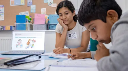 A pupil works on some writing while the tutor looks on