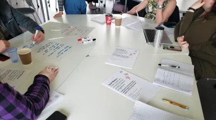 colleagues sit at a table with papers, pens, laptops and coffees