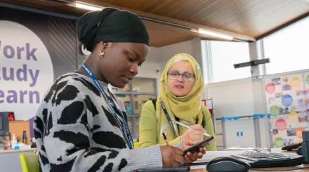 A female college student holds a calculator and is supported by a female tutor a 