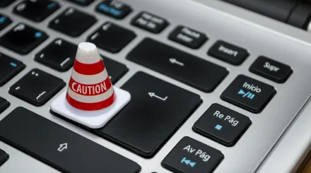 a laptop keyboard close up, with a road cone stating the word 'caution'