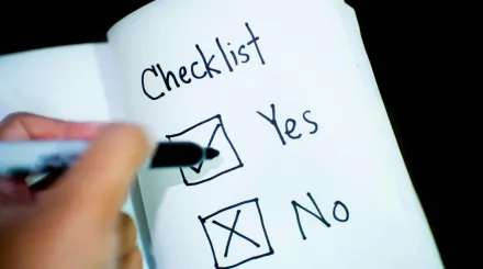 a notebook with a hand marking a checkbox yes with a tick and a cross for a no