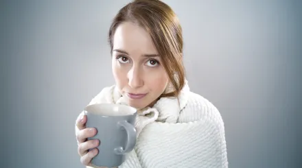 a young woman, wrapped in a white blanket holds a mug