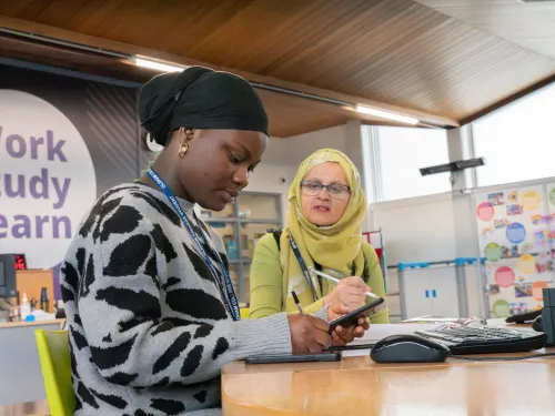 A female college student holds a calculator and is supported by a female tutor a 